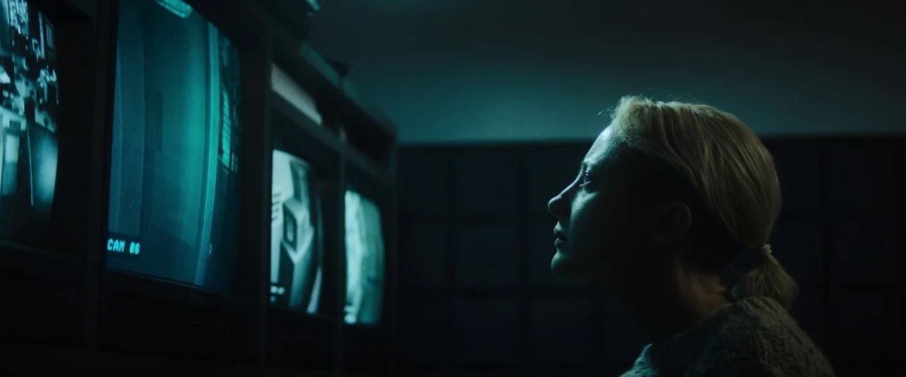 The Grudge (2020) movie still: medium — A dark, dimly lit security room features a row of active CRT monitor screens. A woman stands in profile,…