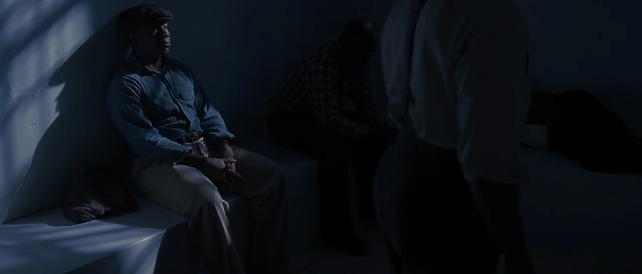 Loving (2016) movie still: medium — A dimly lit room features concrete ledges built against the walls. Two men sit on the ledges while another…
