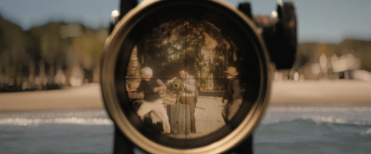 The Bluff (2026) movie still: medium — A sunny beach with light sand and calm water in the background. Three men in period clothing are positioned…