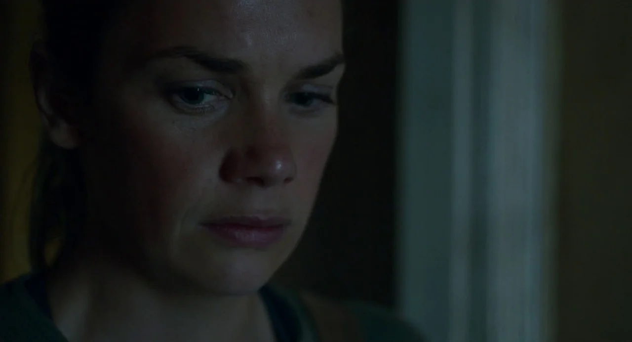 Dark River (2017) movie still: closeup — A dark indoor space with minimal ambient light revealing a person's profile. The subject looks down,…