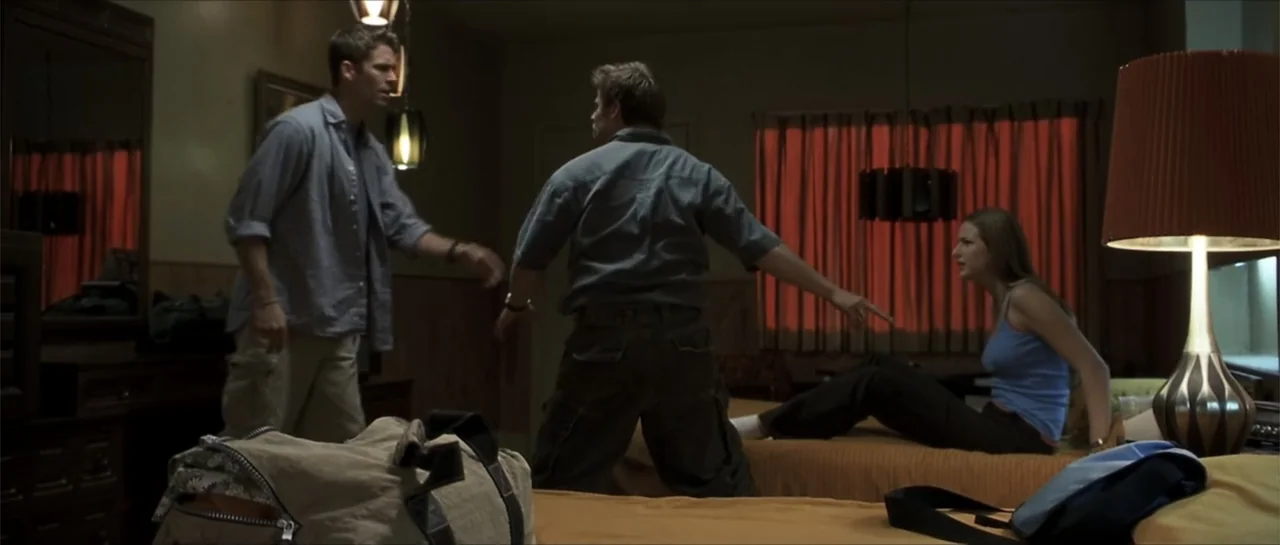 Joy Ride (2001) movie still: fullbody — A dated motel room features two beds with orange spreads and wood paneled walls. Two men stand in the center…