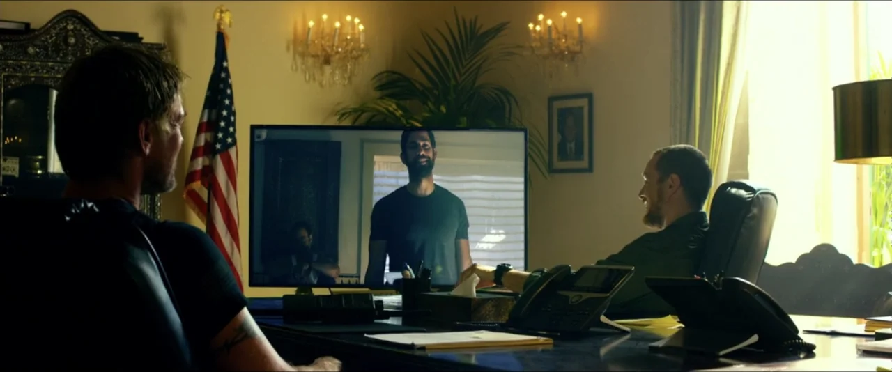 13 Hours: The Secret Soldiers of Benghazi (2016) movie still: medium — An office with an American flag, a potted plant, and a desk telephone. Two…
