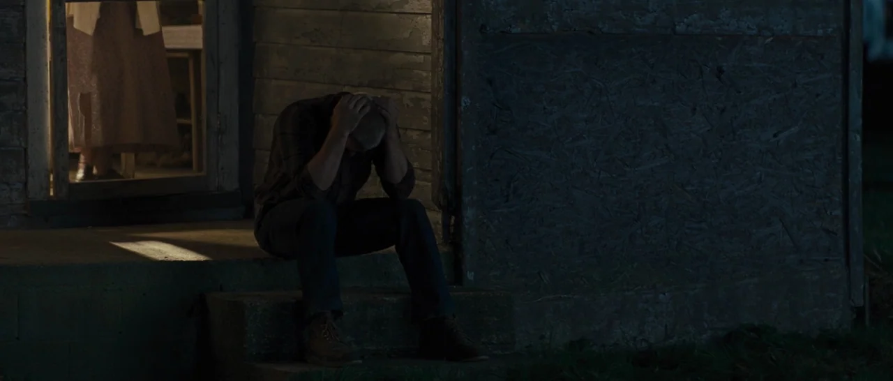 Loving (2016) movie still: medium — A man sits on concrete porch steps in the dark next to a wooden wall. Light glows from an open door behind him…