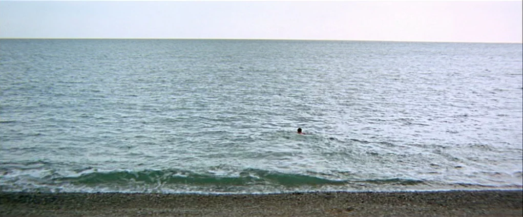 Far from the Madding Crowd (1967) movie still: wide — A vast expanse of sea stretches toward a flat horizon under a pale sky. A lone swimmer is…