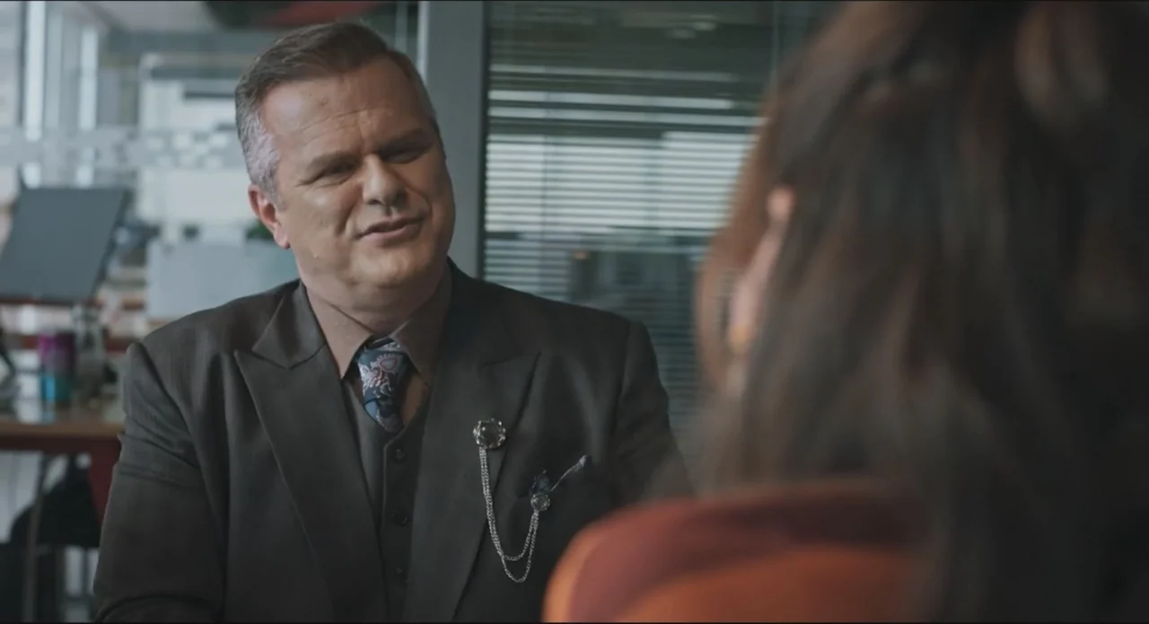 Proof of Love (2022) movie still: medium — A modern office environment features glass partitions and organized desk spaces in the background. A man…