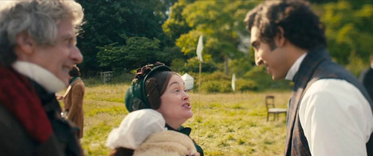 The Personal History of David Copperfield (2019) movie still: medium — An open grassy field during the day with trees in the distant background. A…