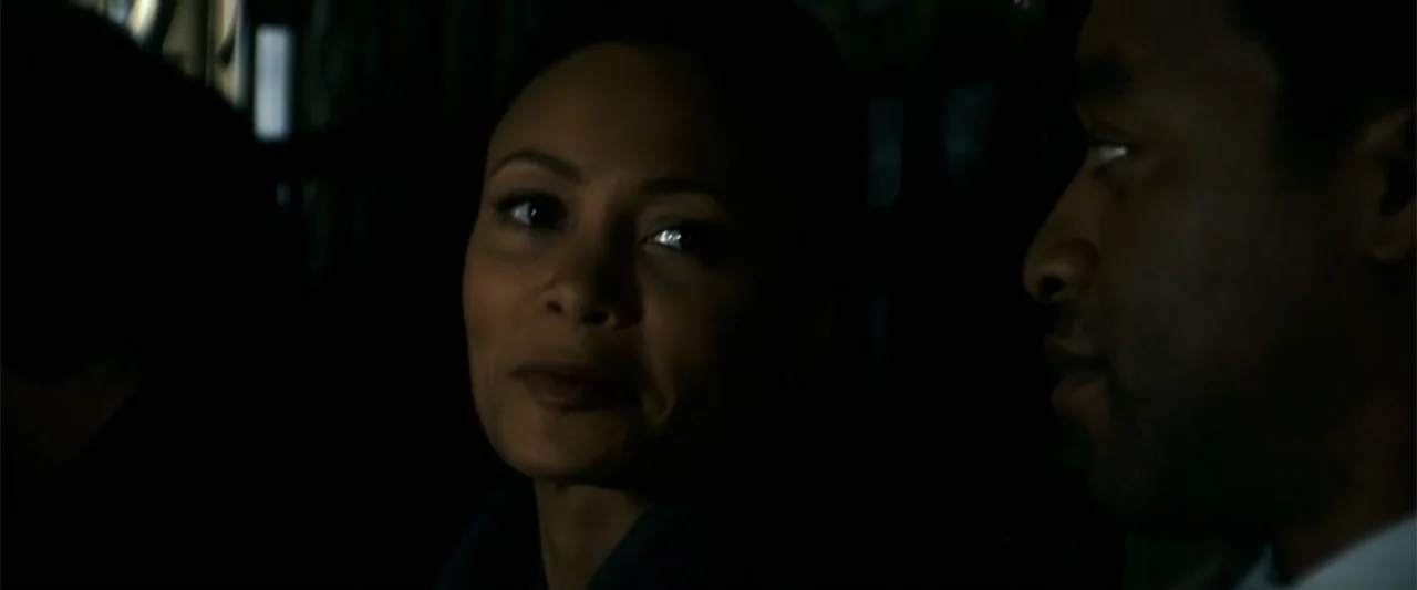 2012 (2009) movie still: closeup — A dark vehicle interior with the faces of a man and woman visible. They are positioned near each other while…