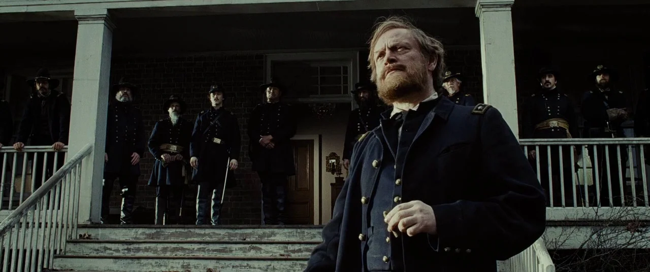 Lincoln (2012) movie still: medium — A historic brick building with white wooden pillars features a wide porch entrance. A bearded man in a dark…