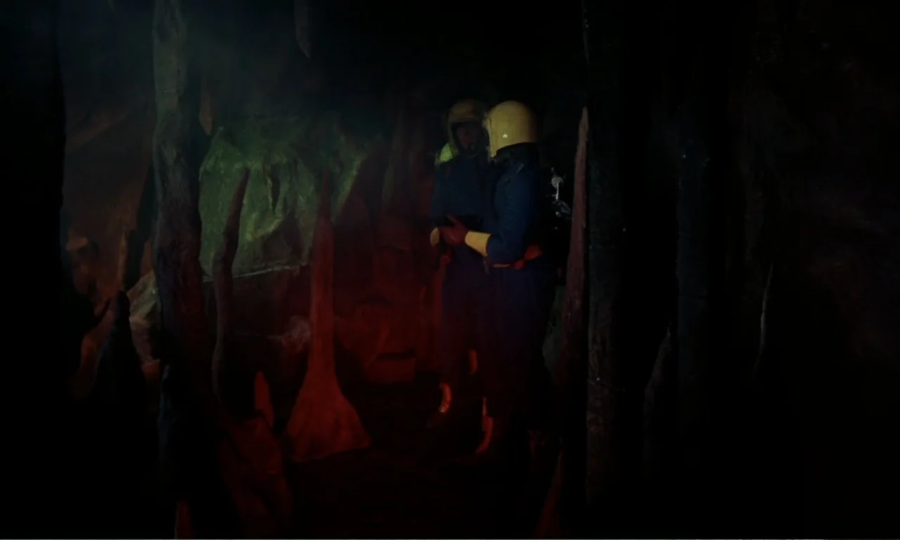 Journey to the Seventh Planet (1962) movie still: medium — A dark cave interior with rock formations and shadows stretching across the walls. Two…
