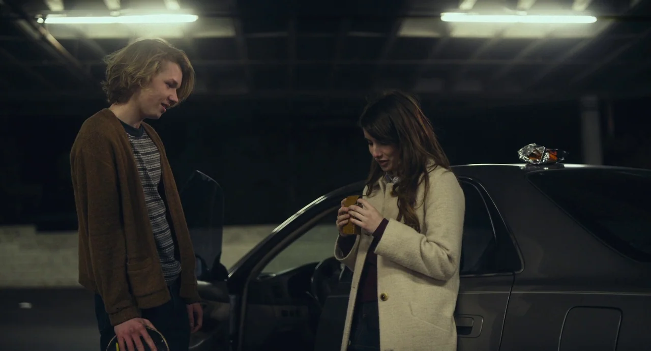 Palo Alto (2013) movie still: medium — A dark, multi-level concrete parking structure with industrial overhead fluorescent strip lighting. A young…