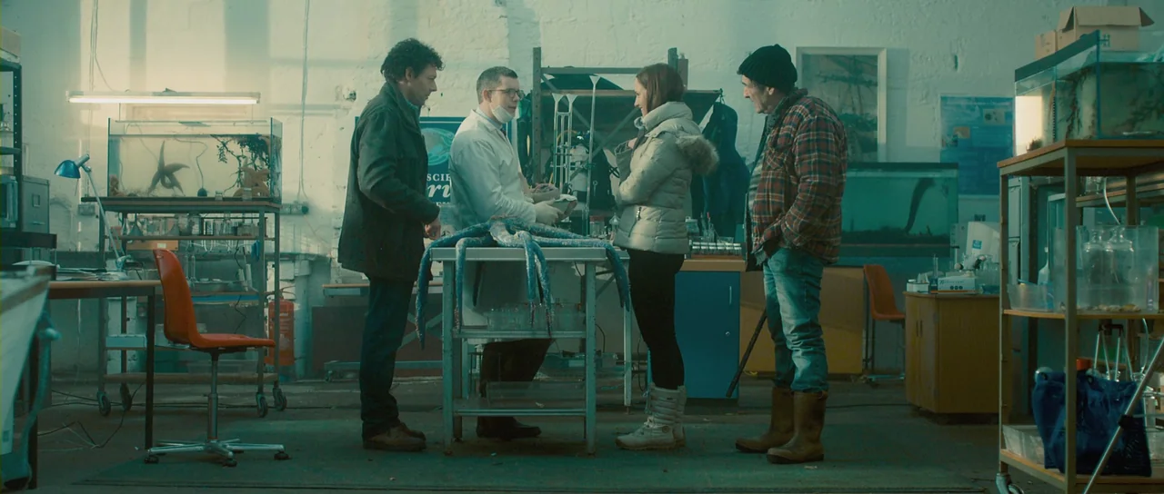 Grabbers (2012) movie still: wide — A cluttered scientific research space features white brick walls and several glass fish tanks. Four people stand…