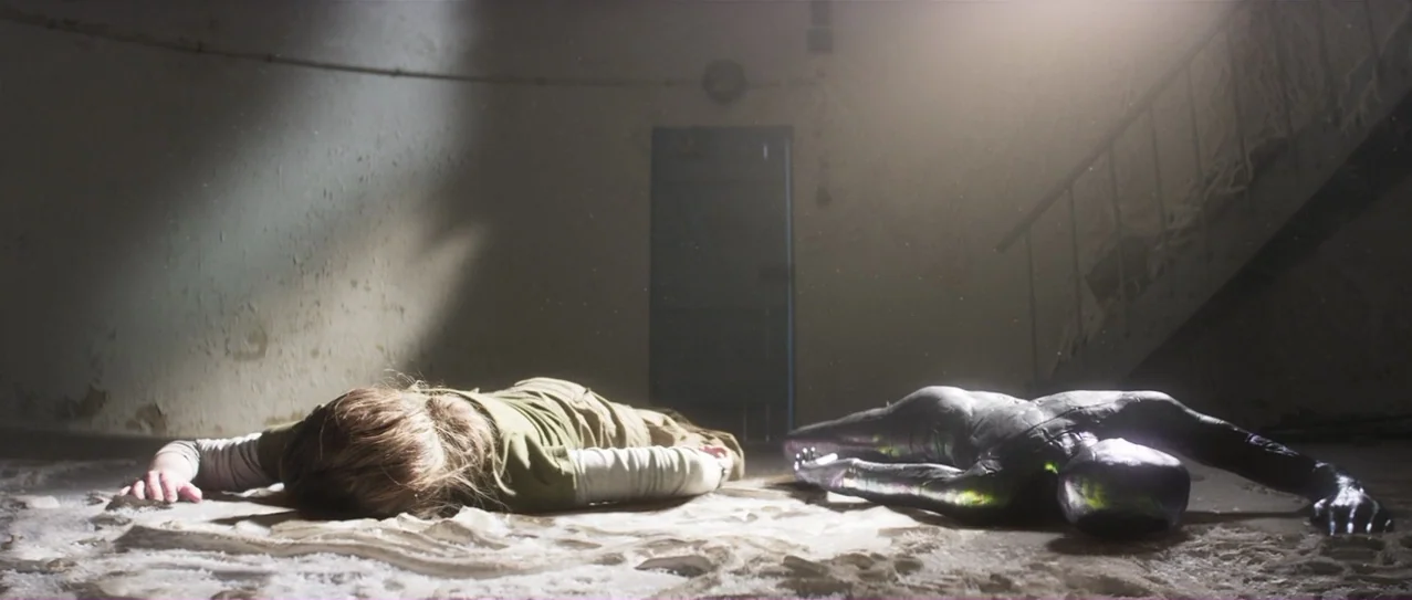 Annihilation (2018) movie still: wide — A dusty concrete stairwell floor contains two bodies lying side by side. A woman in a green shirt rests next…