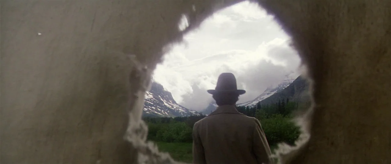 Heaven’s Gate (1980) movie still: medium — A man stands before a mountain range seen through a ragged hole in fabric. The view captures green…