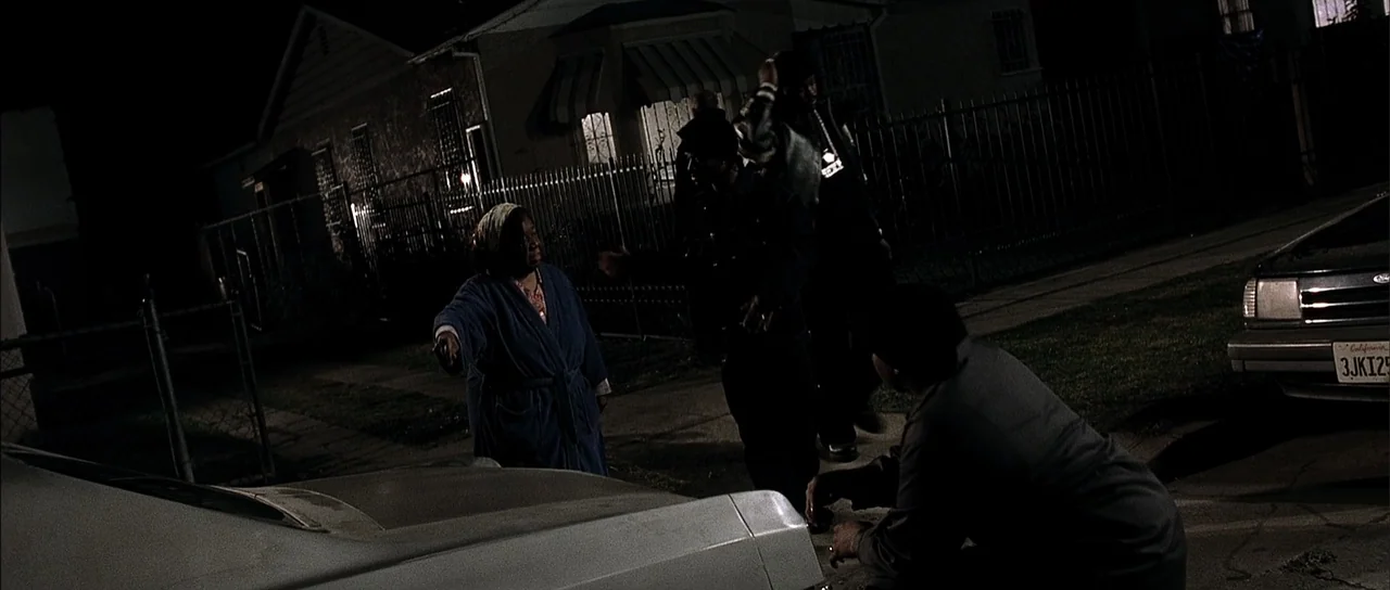A Man Apart (2003) movie still: fullbody — A nighttime suburban scene features a residential house with a gated yard. An older woman interacts with…