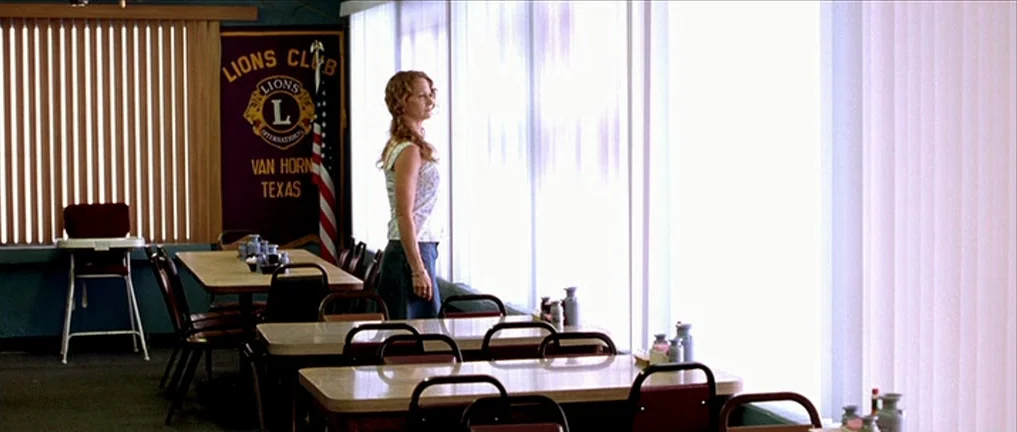 The Three Burials of Melquiades Estrada (2005) movie still: medium — A quiet dining area features tables with red chairs and a Lions Club banner. A…