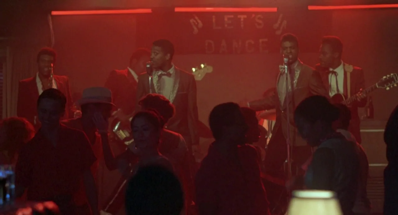 Peggy Sue Got Married (1986) movie still: medium — A dimly lit dance hall features a musical group performing on a small stage. A sign behind the…