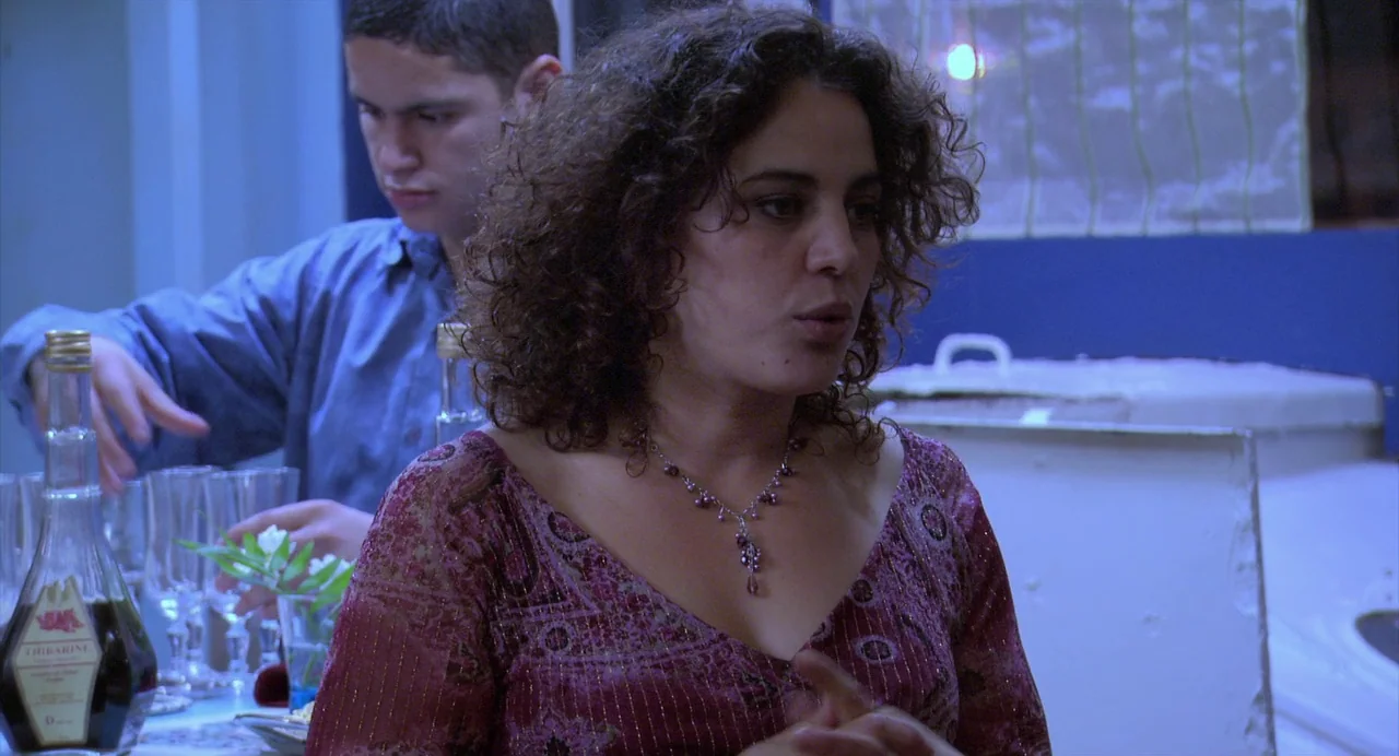 The Secret of the Grain (2007) movie still: medium — A room with blue walls and a white serving counter in the background. A woman in a pink top…