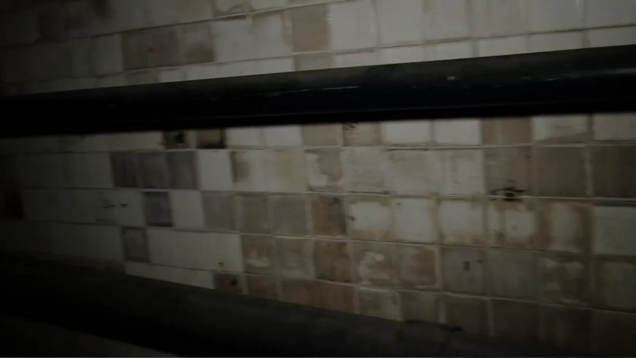 Lost (2010) movie still: establishing — A dark subterranean corridor features aged, stained white square tiles and heavy horizontal piping. No…