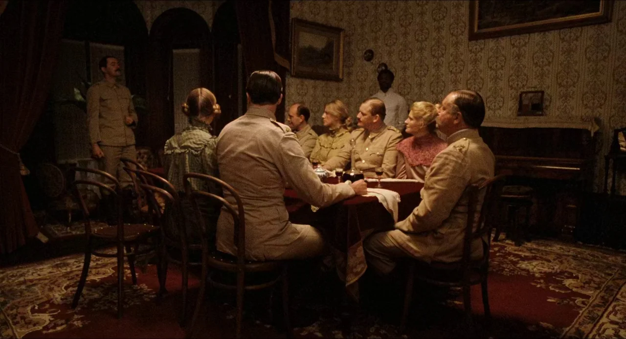 Breaker Morant (1980) movie still: wide — A dimly lit room with ornate wallpaper and heavy dark curtains features a dining table. A group of men in…