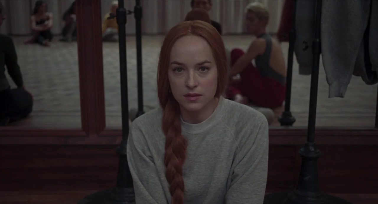 Suspiria (2018) movie still: medium — A dance practice room with wood paneling and large mirrors along the back wall. A woman with long braided red…