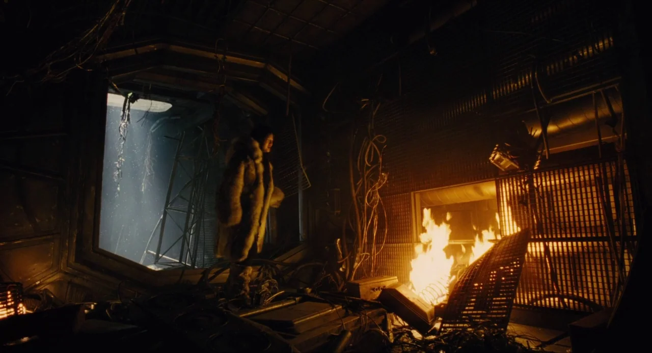Snowpiercer (2013) movie still: wide — A dark, dilapidated metallic room is cluttered with exposed wiring and metallic debris. A person wearing a…