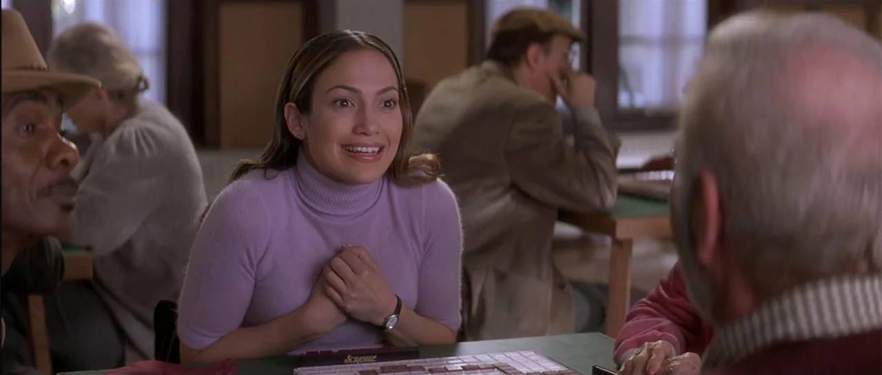 The Wedding Planner (2001) movie still: medium — A room with wooden partitions and tables where people are gathered for a game. A young woman in a…