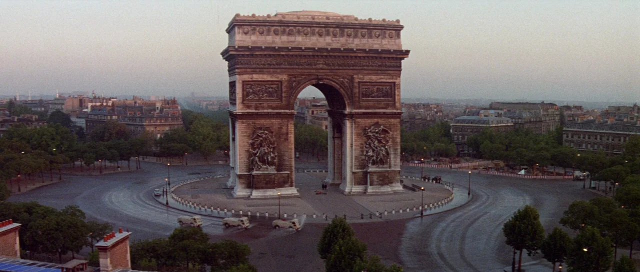 Irma La Douce (1963) movie still: establishing — The Arc de Triomphe sits in the center of a wide, paved traffic circle. Paris city buildings and…