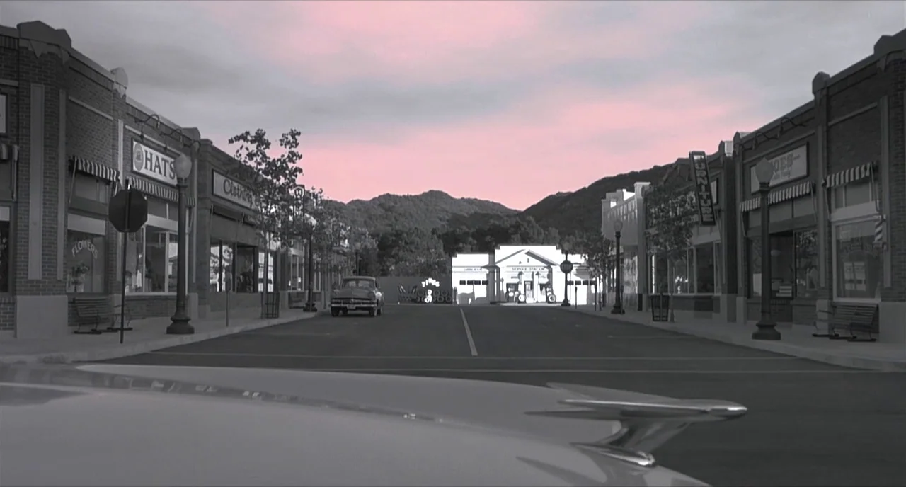 Pleasantville (1998) movie still: establishing — A 1950s style main street with brick storefronts and a service station at the end. An empty road…