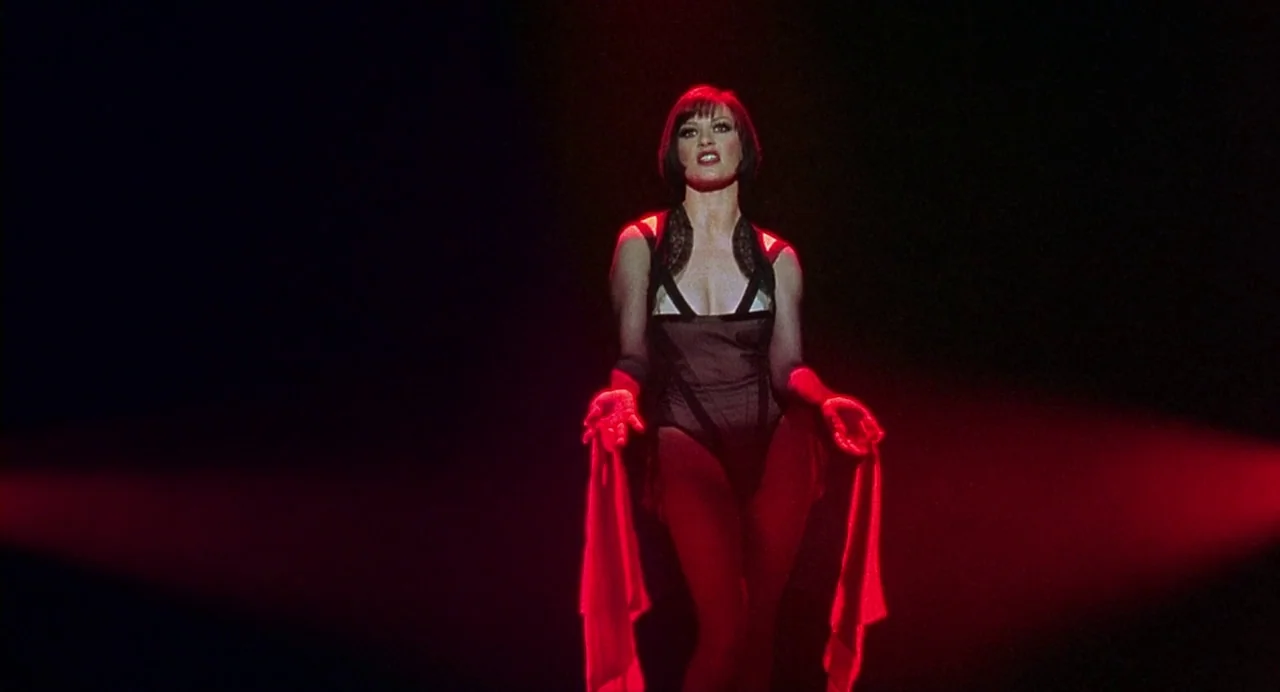 Chicago (2002) movie still: medium — A woman stands on a darkened stage illuminated only by a narrow red spotlight. She is posed with her hands…