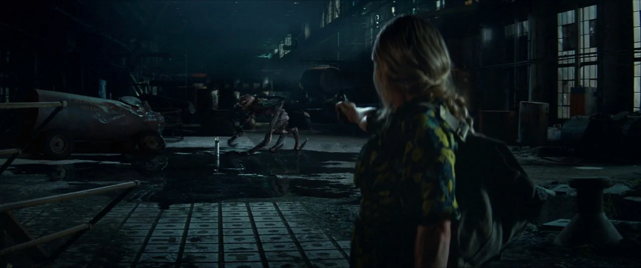 A Quiet Place Part II (2020) movie still: medium — A vast, dark industrial space contains puddles of water and large metal machinery parts. A woman…