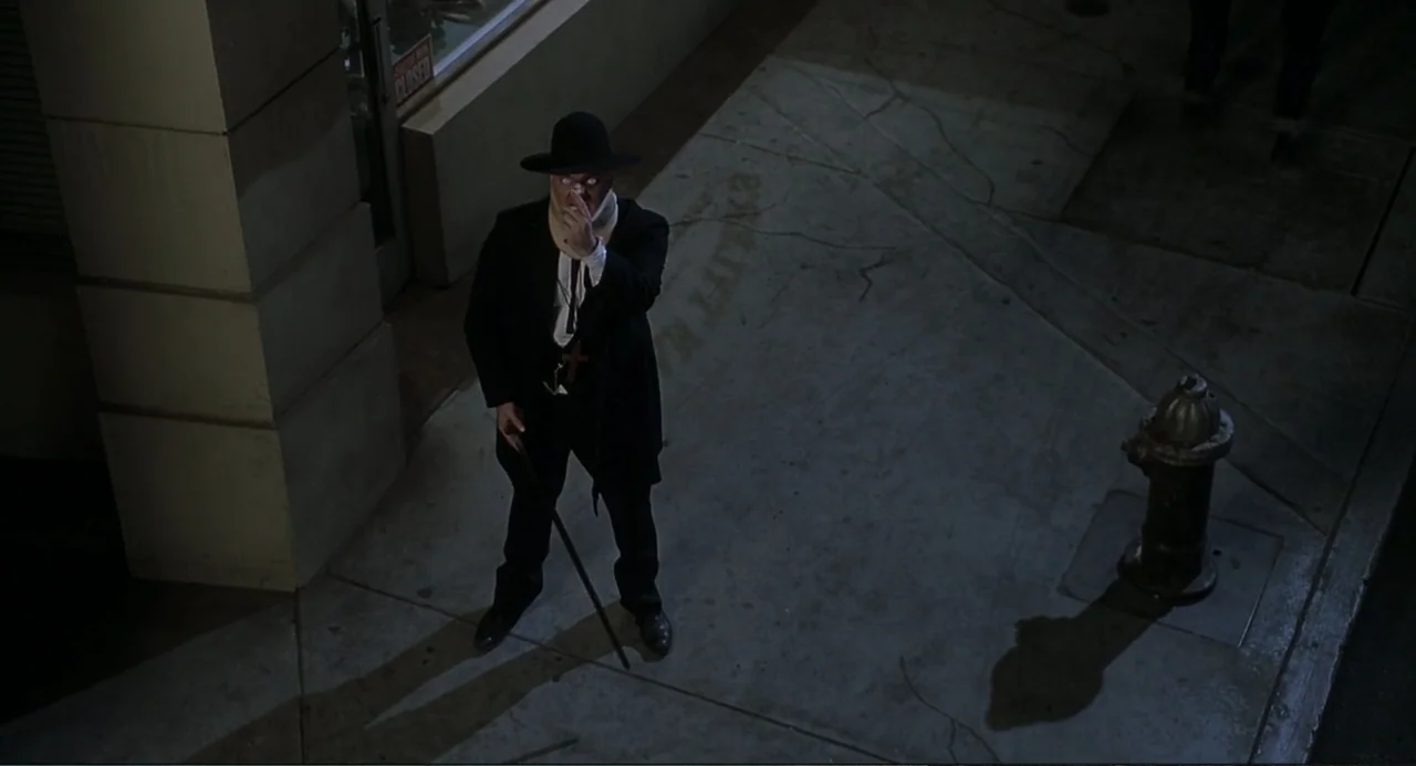Little Nicky (2000) movie still: fullbody — An empty sidewalk at night features a fire hydrant and a large building column. A man in a suit wearing…