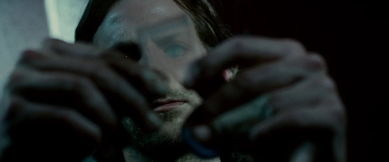 Limitless (2011) movie still: closeup — A man holds a small rectangular object near his face in a dark setting. The focus remains on the translucent…