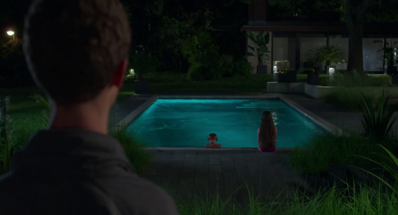 Maps to the Stars (2014) movie still: medium — A nighttime backyard features a illuminated blue rectangular swimming pool surrounded by dark…