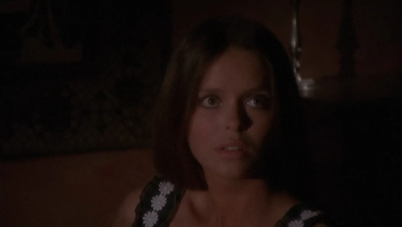 The Black Belly of the Tarantula (1971) movie still: closeup — A dimly lit room provides a dark, obscured background behind the subject. A young…