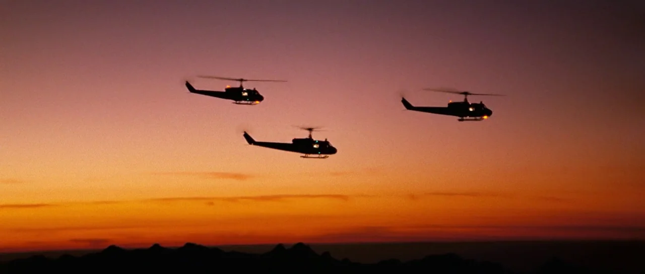 On Her Majesty’s Secret Service (1969) movie still: wide — Three military helicopters are silhouetted against a vibrant, multi-colored sunset sky.…