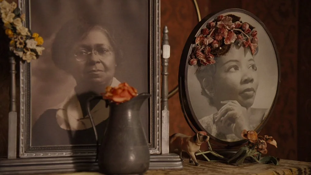 Honeydripper (2007) movie still: closeup — A dark wooden surface holds two framed black and white portraits of women. A small metal pitcher and a…