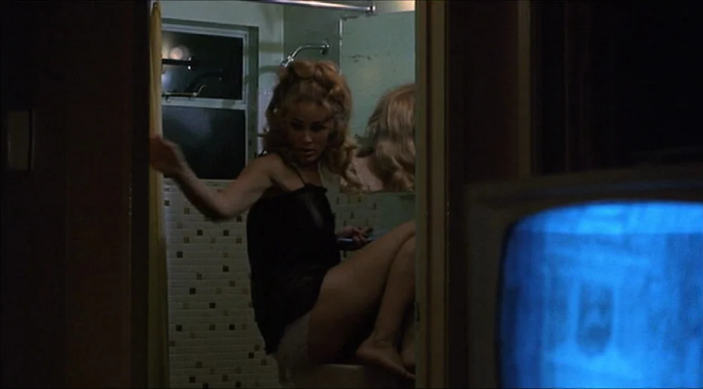 Five Easy Pieces (1970) movie still: medium — A dimly lit tiled bathroom is seen from an adjacent room through a doorway. A woman sits on the edge…