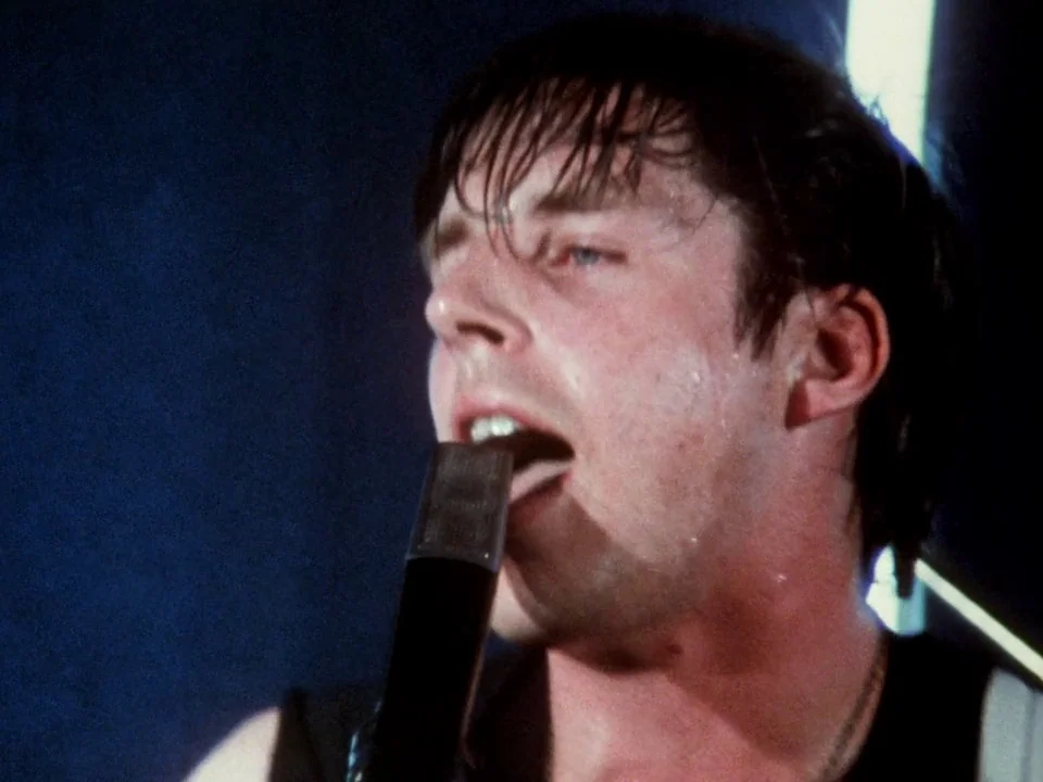 Decline of Western Civilization (1981) movie still: closeup — A dark, minimally lit environment frames a performer under tight stage lighting. A…