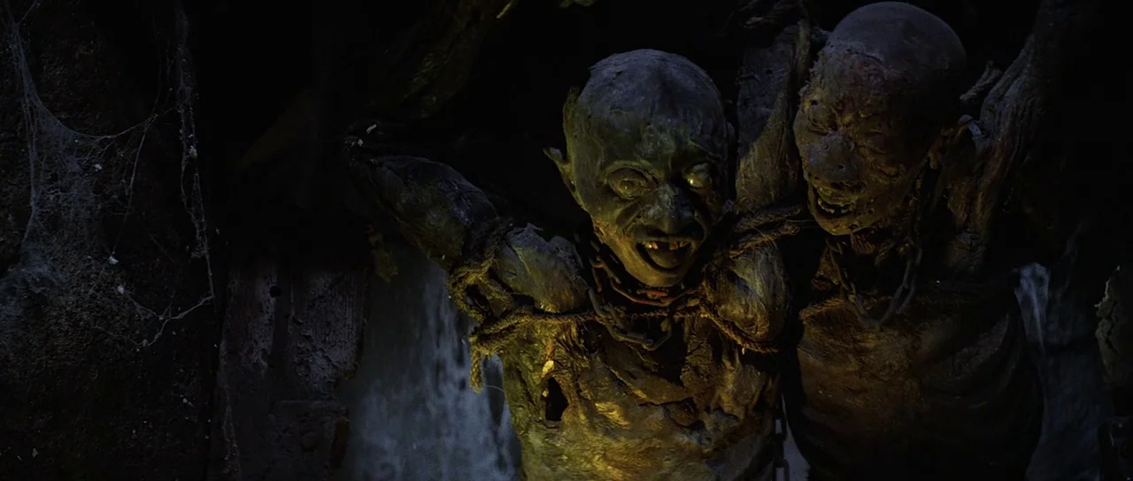 Indiana Jones and the Temple of Doom (1984) movie still: medium — Two green-skinned, gaunt, goblin-like creatures are bound by thick ropes and rusty…