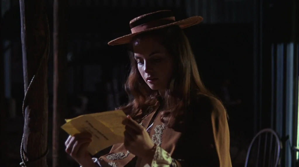 The Ballad of Cable Hogue (1970) movie still: medium — A dimly lit covered porch features a rustic wooden post and a simple chair. A young woman in…