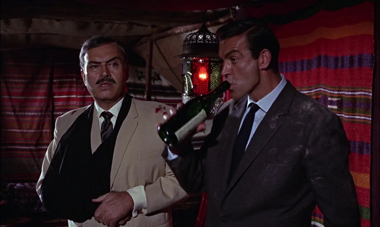 From Russia With Love (1963) movie still: medium — An interior tent space with fabric walls and a hanging ornate glass lantern light. One man holds…
