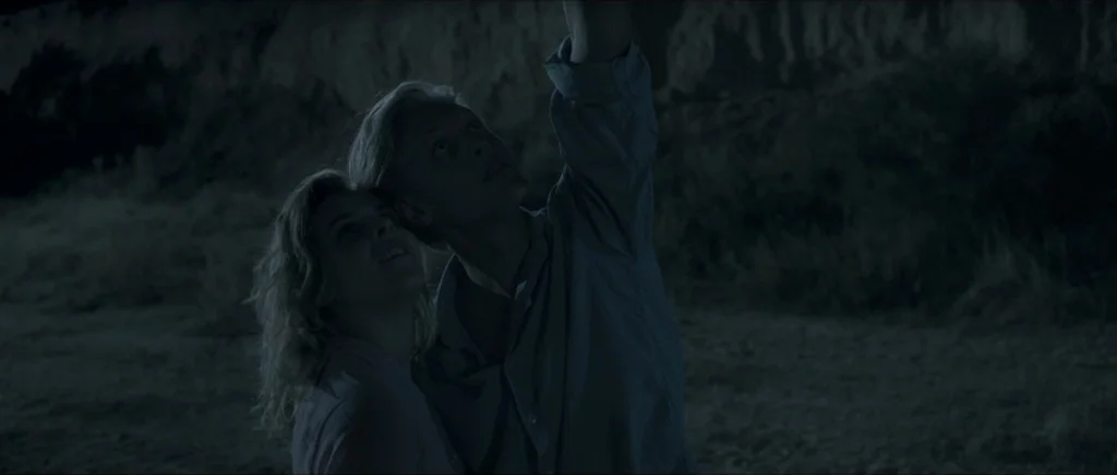 Lasting (Nieulotne) (2013) movie still: medium — A dark night landscape featuring a sandy, uneven terrain beneath a cliff face. A man and woman…