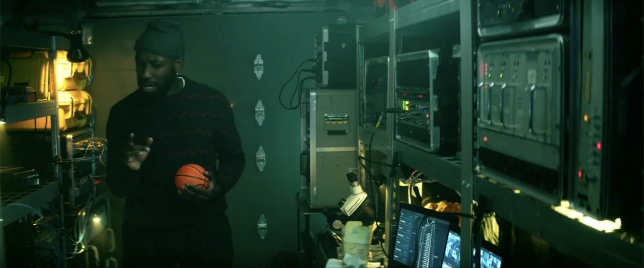 Bloodshot (2020) movie still: medium — A dimly lit technical workspace filled with rows of servers and equipment racks. A man stands between shelves…