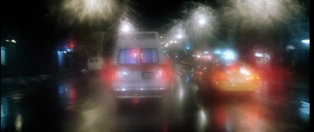 Bringing Out The Dead (1999) movie still: wide — A rain-slicked urban road at night features glowing, smeared lights from passing traffic. An…