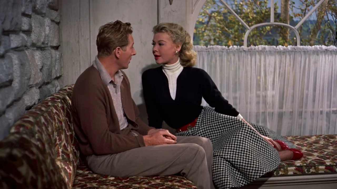 White Christmas (1954) movie still: medium — An interior space features a stone wall and a large window with sheer curtains. A man and a woman sit…