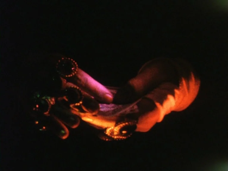 Our Lady of the Turks (1968) movie still: closeup — A pair of hands in the dark are illuminated by a warm light source. The hands hold a stack of…