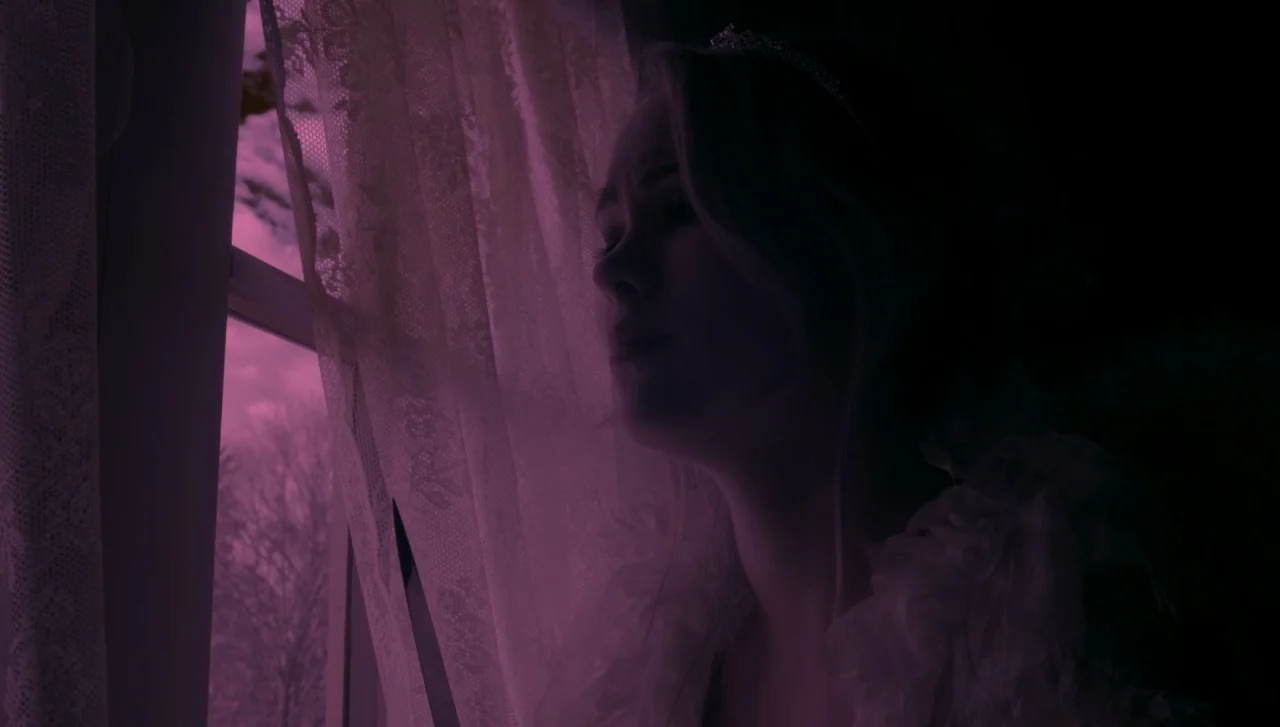 Hellions (2015) movie still: closeup — A dark interior space features a person looking through a window at night. Laced curtains hang beside the…