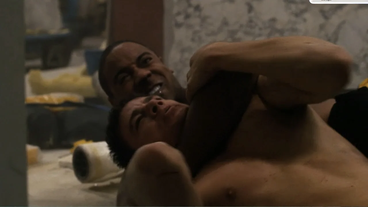 Fighting (2009) movie still: closeup — An unfinished interior space contains exposed concrete and construction supplies on the floor. Two shirtless…