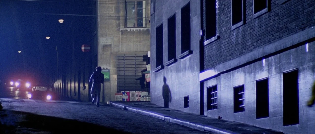 The Bird With The Crystal Plumage (1970) movie still: wide — A quiet urban street at night features a dark brick building on the right. A single man…