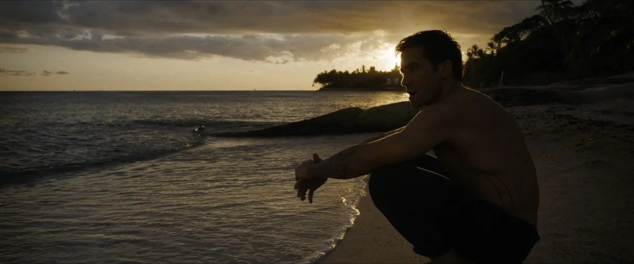 Road House (2024) movie still: medium — A beach shoreline at golden hour with a dark horizon and calm incoming waves. A man in athletic attire…